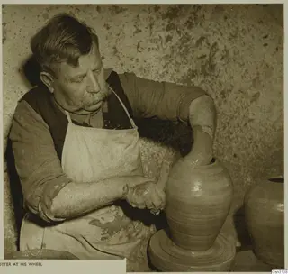 A potter shaping a tall clay vessel on his wheel