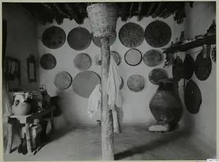 Interior of a room with round woven baskets hung on the walls and a large pottery jar on a stone base