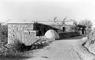 Whitewashed domed oven beside a stone house and dirt track in Cyprus