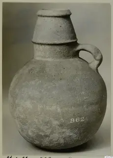 Pottery Plain White IV-V vessel with a round body, tall tapering neck with raised bands, and a single strap handle