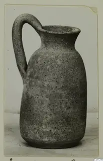 Plain pottery jug with a strap handle and wide mouth, photographed on a pale surface.