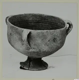 Plain white pottery bowl with two handles on a pedestal foot, photographed against a plain background.