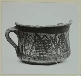 White Painted pottery cup with a loop handle, a dark band under the rim and zigzag and hatched bands on the body