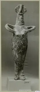 Figurine with arms bent outward and hands at the chest, photographed on a plinth against a grey backdrop