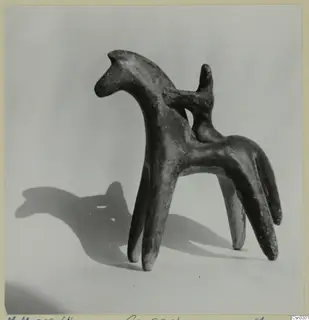 Terracotta figurine of a four-legged animal with a long neck and a small upright stub on its back, shown against a pale background