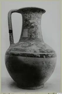 Painted pottery jug with a single loop handle, from Milia, on a pale surface against a grey backdrop