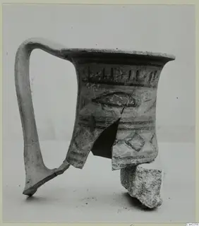 Painted pottery jug with a tall loop handle, decorated with dark bands, a fish-like motif and a lozenge.