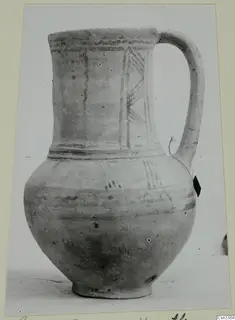 Wheel-made pottery jug with a single handle, painted bands and diagonal hatched strokes on the shoulder.