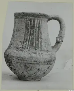 Wheel-made pottery jug with a single loop handle and painted vertical stripes on the body.