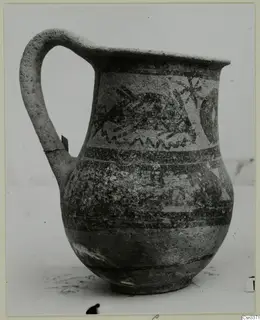 Wheel-made jug with a single handle and painted bands and motifs on its body.