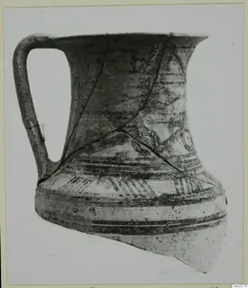 Wheel-made bichrome jug with a strap handle, shown on a card mount