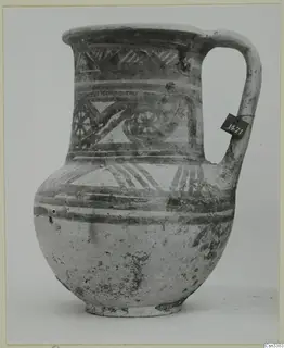 Painted jug with a loop handle, a tall neck and bands of pattern, shown against a plain background.