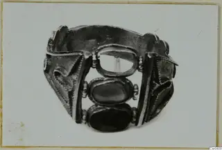 Jewellery: a wide metal band with beaded side panels and three oval settings, two holding dark stones