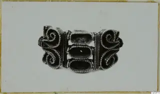 Gold jewellery piece with spiral scrolls and beaded wire edging, shown on a pale card