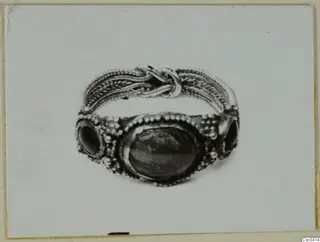 Ring of metal with twisted wire bands, a knot on top, and a dark oval stone flanked by two smaller stones