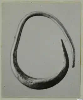 Single open metal ring, oval in outline, one end tapering to a point, photographed on a plain grey backdrop