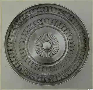Metal dish seen from above, with a central rosette and concentric bands of embossed ornament and small figures