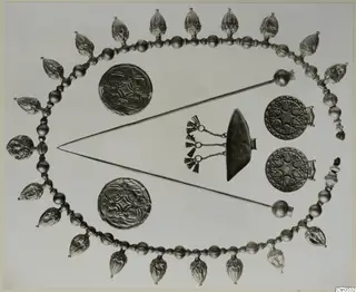Gold jewellery laid out flat: a beaded necklace with pendants, two long pins and several discs.
