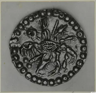 Round gold disc ornament with a raised central motif and a ring of bead-like rosettes around its edge.