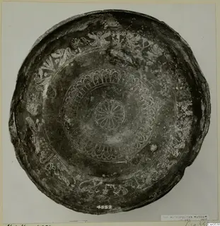 Shallow dark bowl seen from above, with engraved bands of rosettes, birds and animals around the rim