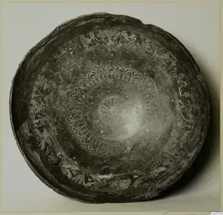 Shallow dark bowl with engraved concentric bands of motifs and a central rosette, photographed from above.
