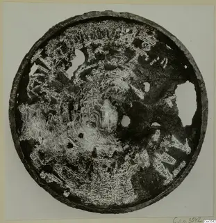 Circular metal bowl seen from above, its dark surface covered with incised figures, animals and patterns