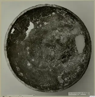 Corroded bowl seen from above, with holes in its surface and incised figures and patterns in the centre