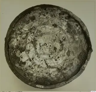 Metal bowl seen from above, its interior decorated with incised animal friezes and concentric bands of dots.