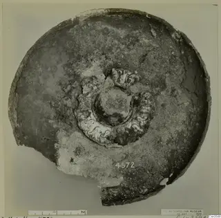Shallow round vessel seen from above, with a raised central boss ringed by pale scroll-like relief ornament