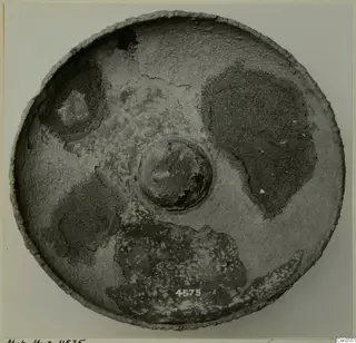 Round bowl seen from above, with a raised central boss and a mottled, worn surface