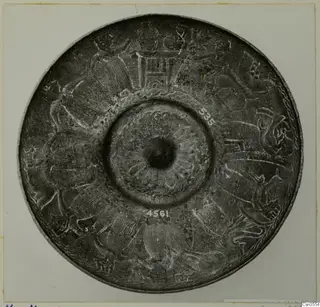Round metal dish seen from above, with engraved figures and animal-like forms around a central boss