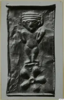 Embossed metal plaque with a standing figure wearing a banded headdress, above a cluster of rounded lobed shapes.