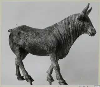 Bronze figure of a horned animal standing in profile, facing right, with four legs and hooves