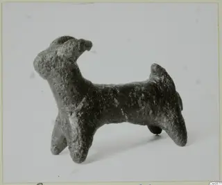 Small bronze figurine of a four-legged animal with raised head and upturned tail, in side view