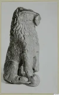 Small bronze figure of a seated animal with a mane, shown from a side view against a plain background