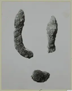 Three corroded metal pieces on a pale background: two elongated fragments and a small irregular lump.