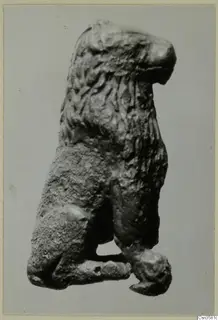 Bronze figure of a maned animal with its head raised, photographed against a plain grey background