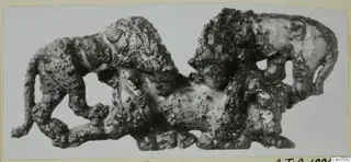 Bronze sculpture of two lions attacking a bull, with a heavily corroded surface