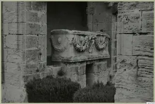 Stone sarcophagus with a carved garland band, standing in a recess between stone block walls