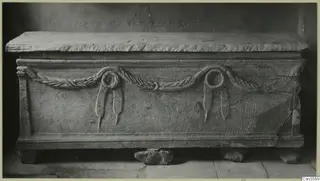 Stone sarcophagus with a carved garland and two knotted ribbons across its front panel
