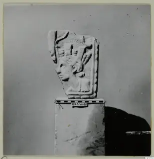 Relief fragment showing a head in profile with an elaborate headdress, set on a stone block with a scale bar beside it.