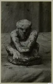 Small limestone figurine of a seated, crouching figure with knees drawn up and head bowed, on cloth.