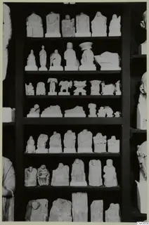 Rows of small limestone figures and fragments displayed on dark wooden shelves