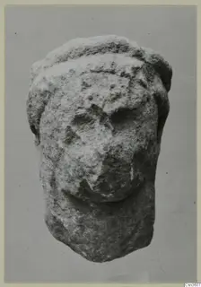 Limestone statuette fragment of a head with a band across the top, face worn away, shown against a grey backdrop