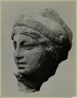 Carved marble head of a figure with a band across the brow and downcast eyes, photographed against a plain background.
