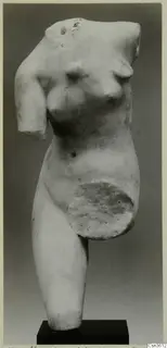 Marble sculpture of a female torso, headless and missing its arms, standing on a dark rectangular base.