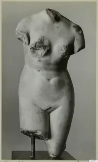 Marble torso of a standing human figure, headless and armless, mounted on a metal stand against a grey backdrop.