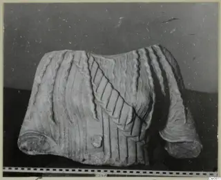 Marble sculpture fragment with carved wavy ridges and grooved bands, a rolled edge at each end, shown with a scale bar.