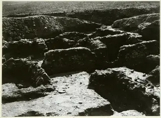 Excavated stone wall foundations and a stony floor surface in a dug area, seen from above.