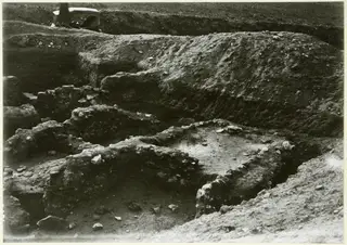 Excavation trench with exposed stone walls and rubble, with a partly visible person at the top left edge
